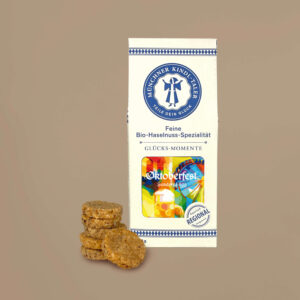 Kleine Cremefarbe Schachtel mit blau bedrucktem Text. Sichtfenster zeigt das original Oktoberfest Motiv 2026 von Florian Huber. 100 Gramm.